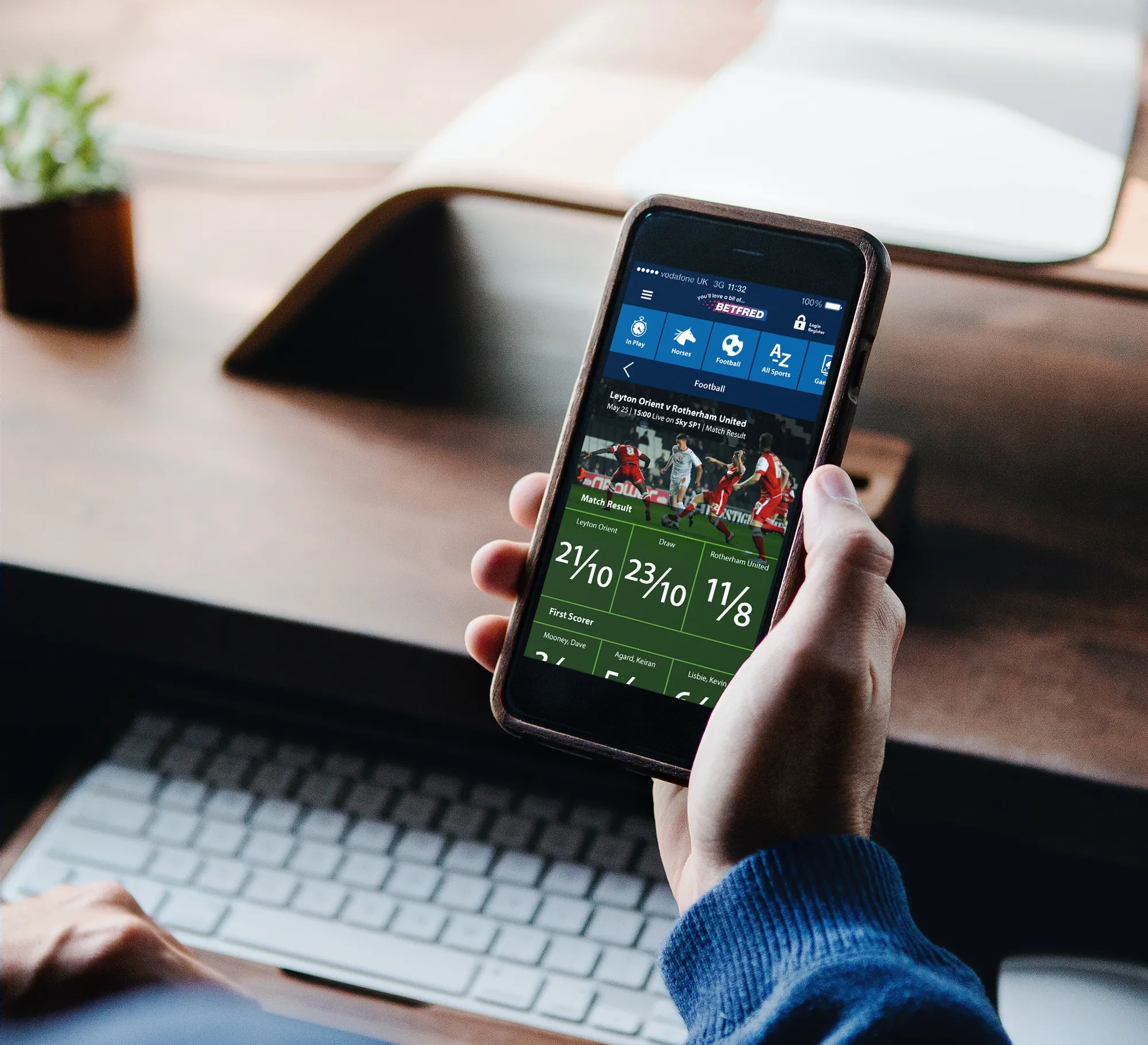 The Betfred app in one hand at a desk, football match odds on screen