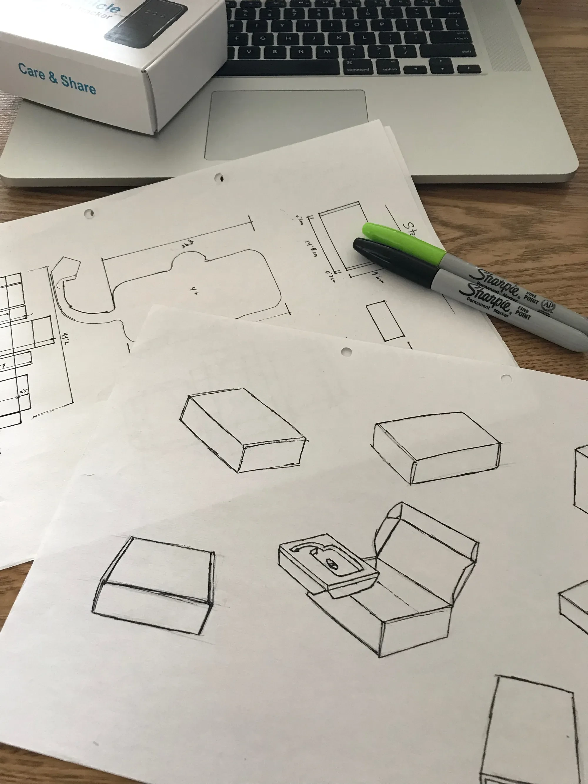 Structural sketches and a die-line drawing on the desk, marker and laptop alongside